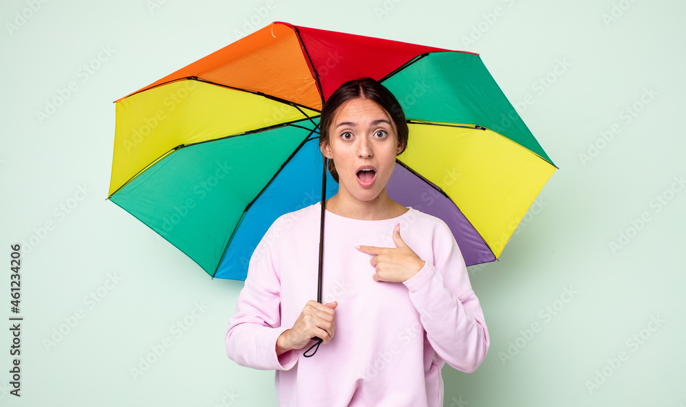 Poster young pretty woman looking shocked and surprised with mouth wide open, pointing to self. umbrella concept