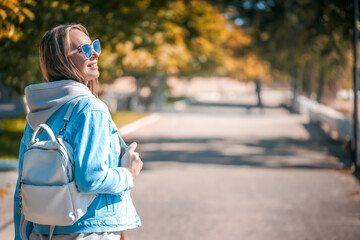 Young beautiful woman walks outside in stylish casual outfit with leather backpack in autumn.