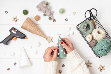 Christmas craft hobby background with handmade yarn cone xmas trees in natural colors. Recomforting, destressing hobby to make christmas decoration. Top view of diy workshop