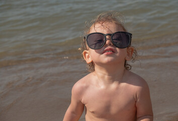 A small child of 1.6 years old put on big sunglasses on the beaches and smiles.