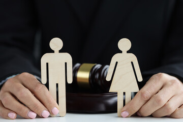 Wooden figures of man and woman in hands of judge against background of judge hammer