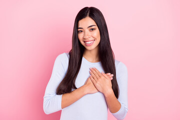 Photo portrait of girl smiling thankfully keeping hands on heart isolated on pastel pink color background