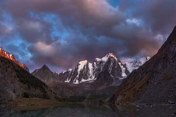 Darkness mountain landscape with great snowy mountain lit by dawn sun among dark clouds. Awesome...