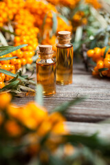 Natural oil of sea buckthorn (Hippophae) in glass bottle with fresh, juicy ripe yellow berries on a wooden background