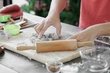 Selective focus on ginger man mold that a little girl's hands are pressing onto cookie dough. Little kid making Christmas ginger cookies in kitchen decorated with Christmas tree at home