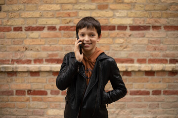 hoto of teenage boy aged 11-12 is talking on smartphone against background of brick wall in the city, smile on his face