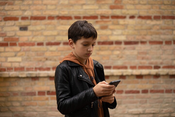 Photo of teenage boy aged 11-12 using smart phone against background of brick wall in city