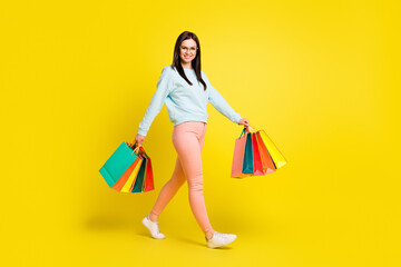 Profile full body photo of nice brown hairdo young lady go with bags wear spectacles hoodie trousers isolated on yellow background