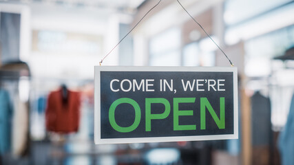 Shot of a Sign "We are Open" on a Glass Door of a Stylish Clothes Store. Blurred Background of a Shop, Supermarket, Bar or Another Company, Business.
