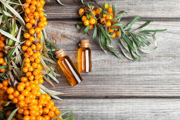 Natural oil of sea buckthorn (Hippophae) in glass bottle with fresh, juicy ripe yellow berries on a wooden background. Top view