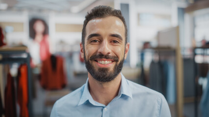 Obraz premium Portrait of a Happy Handsome Store Assistant in Blue Shirt Smiling and Posing for Camera at Clothing Store. Small Business Owner in a Role of a Businessman or Sales Manager.