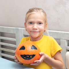 The girl shows a pumpkin with a painted scary face, creating a Halloween Jack Lantern. Halloween party