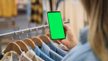 Clothing Store: Female Using Smartphone with Chroma Key Green Screen Display. Clothes Hanger with...