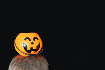 Orange basket in the shape of a pumpkin with a grinning face, Jack's lantern on a child's head isolated on black