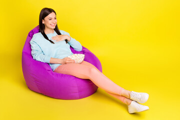 Full length body size photo girl laying in beanbag watching movie eating pop corn isolated vibrant yellow color background