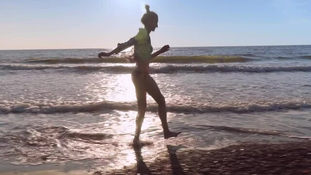 A slender woman runs and jumps on the waves of sea water on a sandy beach. on the surf. Splashes of water and foam on the background of the orange sun at sunset. Caucasian beauty is happy and joyful.
