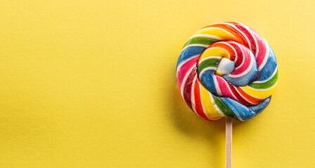 Sweet round lollipop with rainbow colour on the wooden stick with yellow background