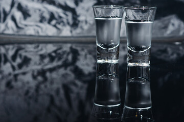 Close-up view of bottle of vodka with glasses standing on ice on black