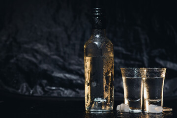 Close-up view of bottle of vodka with glasses standing on ice on black