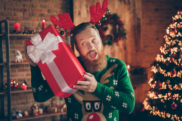 Portrait of attractive cheerful amazed guy holding giftbox having fun eve day at modern loft...