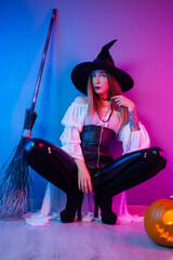 a girl in a witch costume for Halloween with a broom and a pumpkin in neon light
