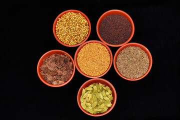 Top view of Indian spices, Fenugreek seeds, Coriander seeds, Cardamom-Black, Cardamom-Green, Cumin seeds, Mustard seeds in clay bowls on a Black Background, Maharashtra