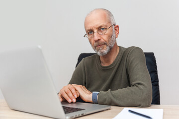 Adult man with gray hair working on laptop and looking at camera
