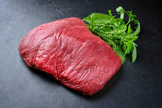 Raw dry aged bison beef rump steak piece as close-up with herbs on black background with copy space