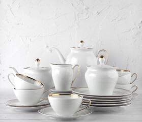 White tea set on a white background. Teapot, cream, sugar bowl, cups, saucers, plates on the table. Porcelain dishes. For six persons.

