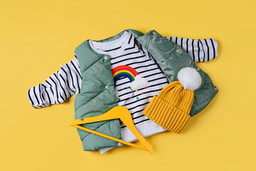 Waistcoat down jacket with striped jumper on yellow background. Stylish childrens outerwear....