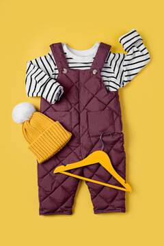 Warm pants and striped jumper  with hat on yellow background. Set of baby clothes for winter. Fashion kids outfit.