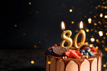 Chocolate birthday cake with berries, cookies and number eighty golden candles on black background,...