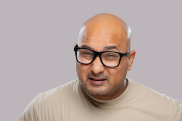 Portrait of a bald man wearing eyeglasses with confused expression against plain background.