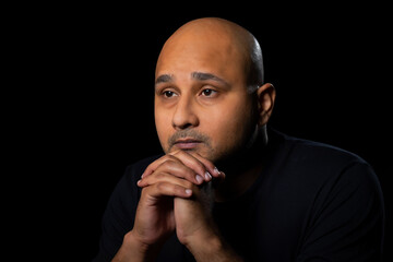 Portrait of a bald man gazing with an anxious tensed look against dark black background.