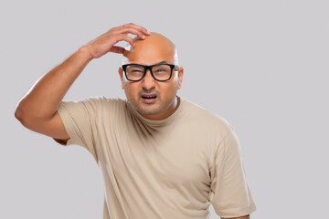 Portrait of a bald man wearing eyeglasses scratching his head with confused expression against...