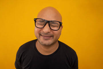 Portrait of a bald man wearing eyeglasses smiling against plain background with closed eyes.