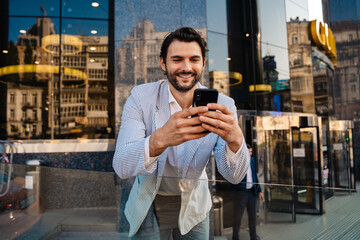 Young man wearing jacket smiling and using mobile phone