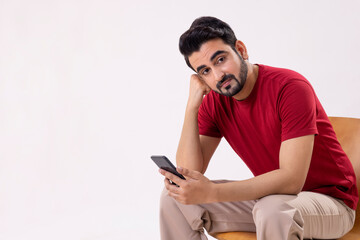 PORTRAIT OF A MAN SITTING WHILE HOLDING MOBILE PHONE AND LOOKING AWAY
