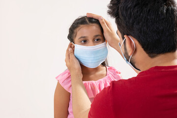 A FATHER CAREFULLY CHECKING FACE MASK OF DAUGHTER TO PROTECT FROM PANDEMIC