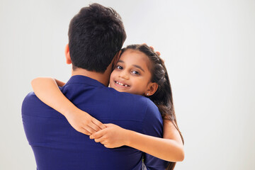 A YOUNG GIRL LOOKING AT CAMERA WHILE EMBRACING HER FATHER