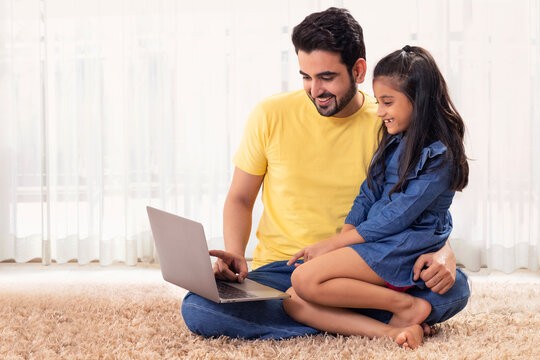 A FATHER SITTING AND SHOWING LAPTOP TO DAUGHTER