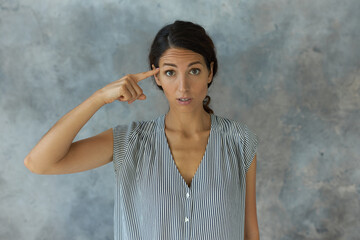 Studio shot of confident beautiful brunette woman in striped sleeveless shirt holding finger near...