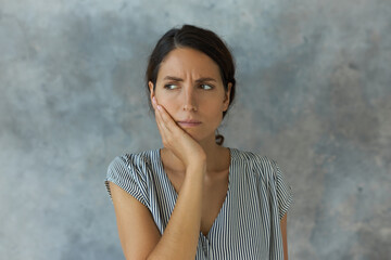 Frowning female of 30s pressing her cheek with painful face expression, having terrible tooth ache,...