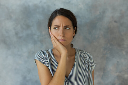 Frowning female of 30s pressing her cheek with painful face expression, having terrible tooth ache, looking aside trying to think of something to avoid pain. Dental health and care