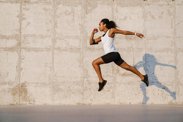 Black sportswoman listening music while working out on parking