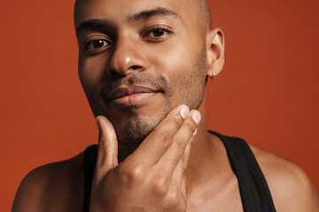 Black bold man wearing shirt rubbing his chin while looking on camera