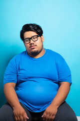 Porrait of a fat man wearing eyeglasses sitting with a dull tired expression on face.