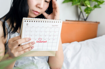 stressed Asian woman looking at  calendar having problem with menstrual cycle waiting for ovulation day - obrazy, fototapety, plakaty