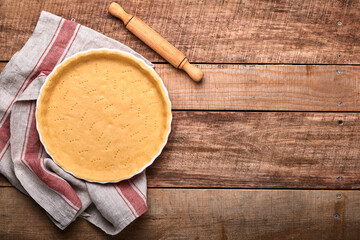 Dough for baking quiche, tart or pie in ceramic baking form ready for bake on kitchen towel over old rustic plank wooden background. Top view, copy space. Concept homemade baking for holiday.