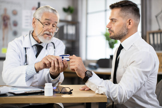 Competent senior doctor using finger pulse oximeter for testing oxygen level in blood of caucasian man in business wear. Concept of people, examination and treatment.